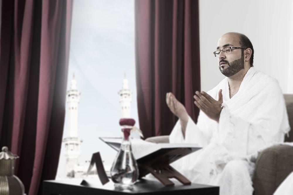 マカレム アイヤッド メッカ ホテル エクステリア 写真 The photo depicts a man sitting in a room, wearing traditional white garments typically associated with the Hajj pilgrimage. He appears to be engaged in a prayer or spiritual practice, with his hands raised in a gesture of supplication. In the backgr