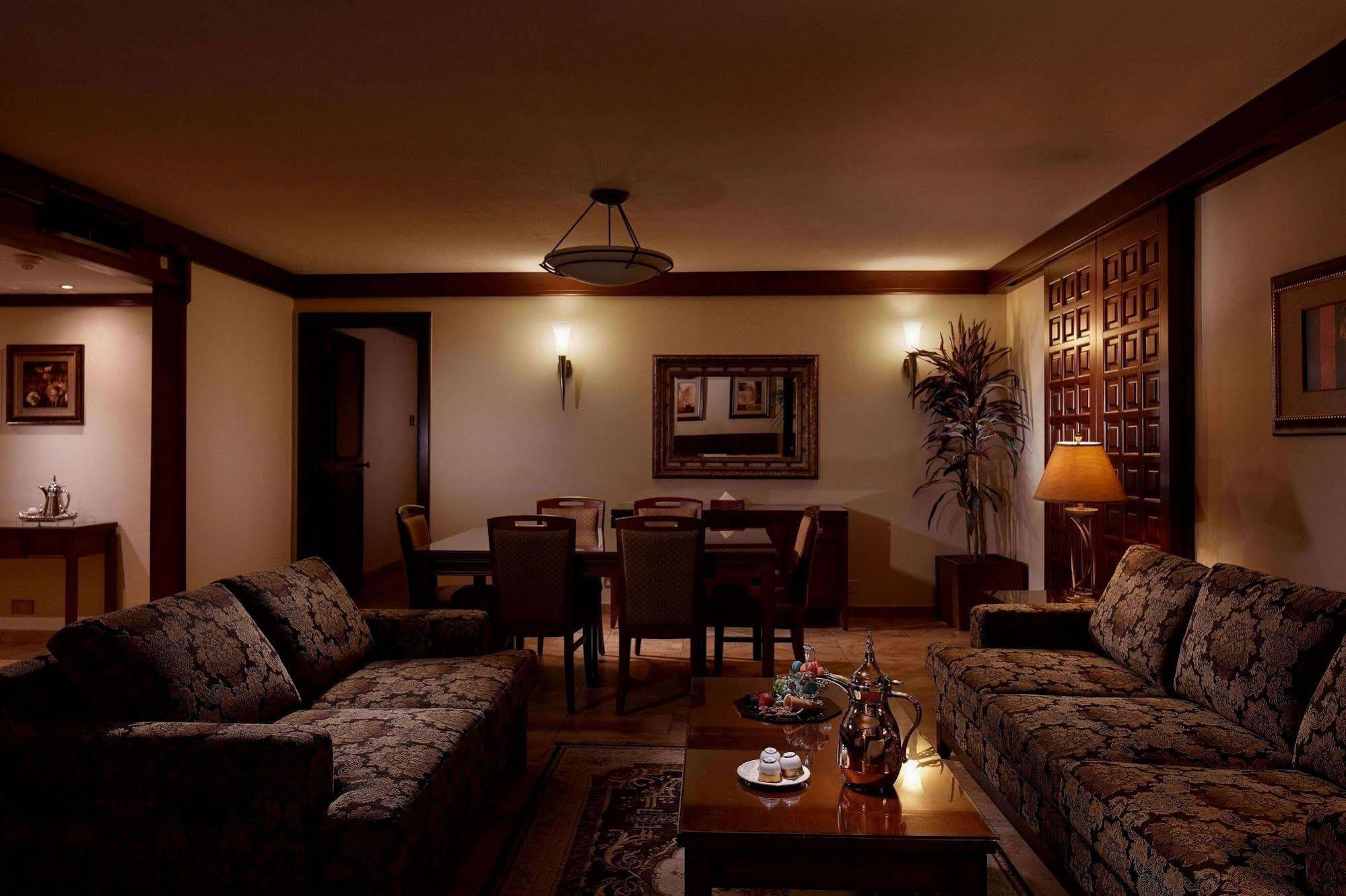 マカレム アイヤッド メッカ ホテル エクステリア 写真 The photo depicts a cozy living room setting. It features two patterned sofas facing each other with a wooden coffee table in the center. The room is softly illuminated, creating a warm atmosphere. On the walls, there are decorative elements, includi