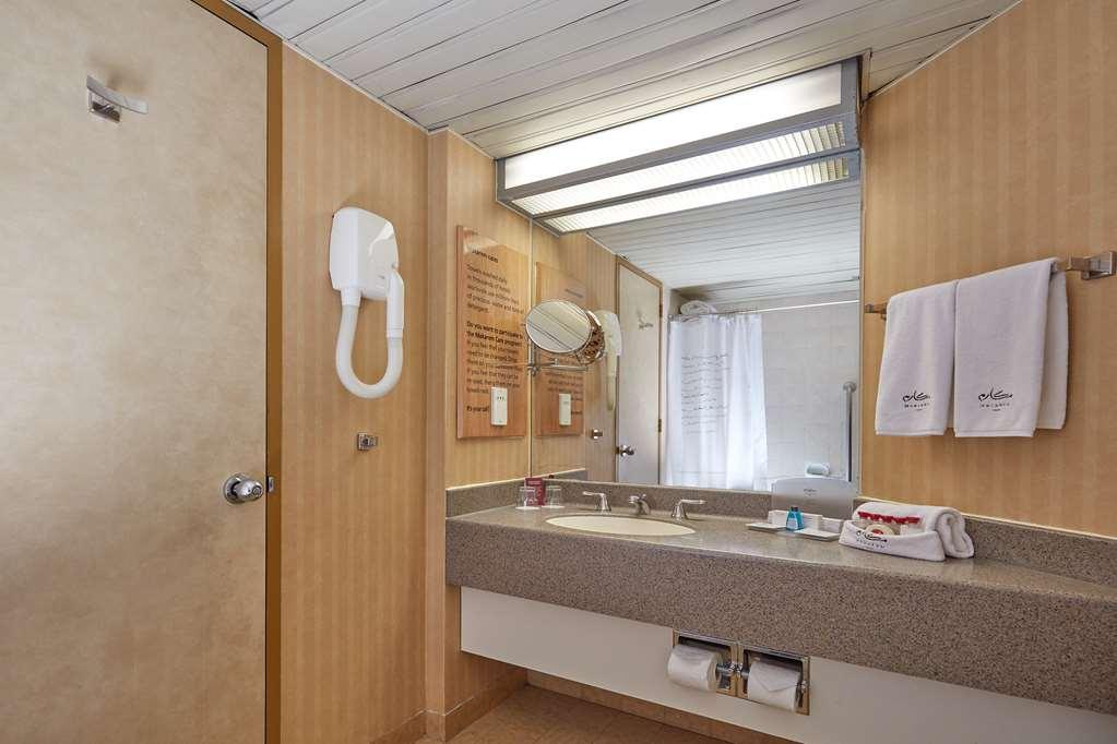 マカレム アイヤッド メッカ ホテル エクステリア 写真 The photo shows the interior of a bathroom. It features a light-colored wall with vertical stripes and a ceiling that is white and textured. There is a gray countertop with a sink and a mirror above it. On one side, there are two white towels hanging