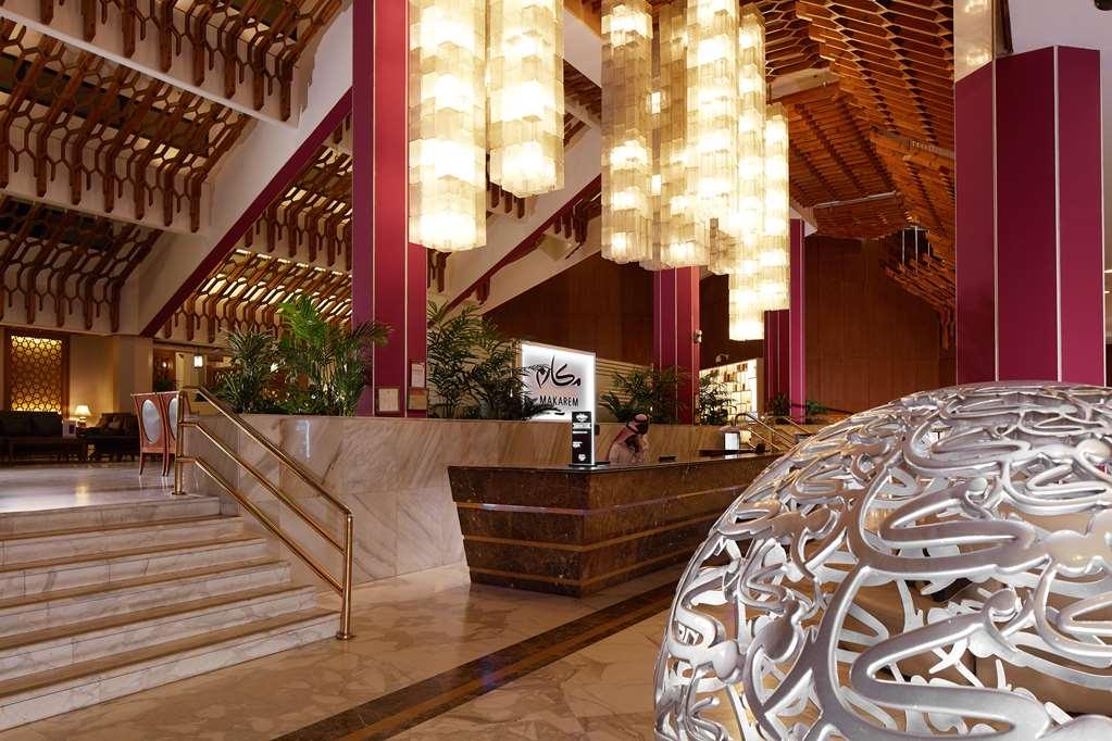 マカレム アイヤッド メッカ ホテル インテリア 写真 The photo depicts a luxurious hotel lobby. It features a grand entrance with a staircase leading up to a reception area. The lobby has high ceilings adorned with striking, modern light fixtures that hang down, providing a warm ambiance. The walls are