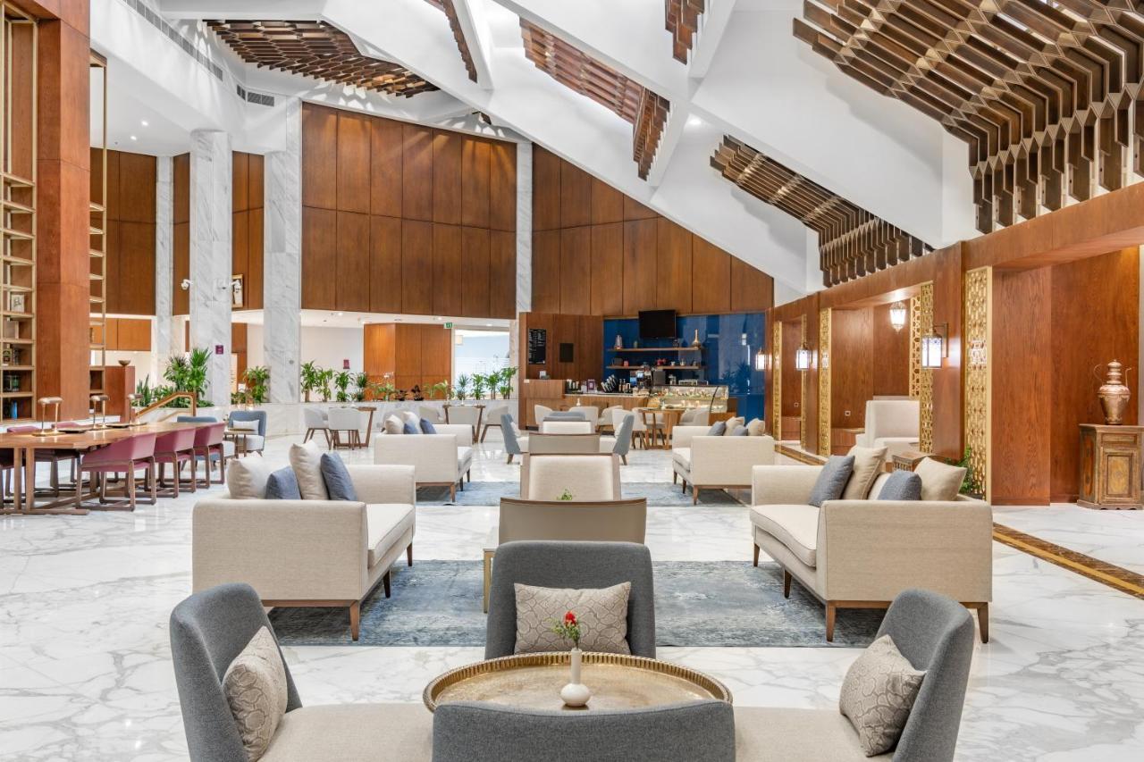 マカレム アイヤッド メッカ ホテル エクステリア 写真 The photo depicts the interior of a modern and elegantly designed lobby or lounge area. It features a spacious layout with high ceilings, showcasing a combination of wooden elements and marble flooring. 

In the center, there are several seating arra