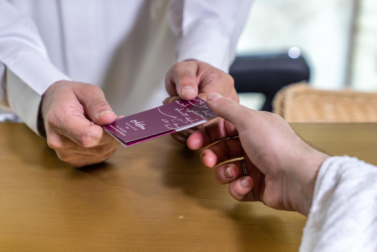 マカレム アイヤッド メッカ ホテル エクステリア 写真 The photo shows two hands engaged in a transaction. One hand is extending a card towards another hand. The person handing over the card appears to be wearing a white garment, possibly a shirt or robe, while the person receiving the card has their han