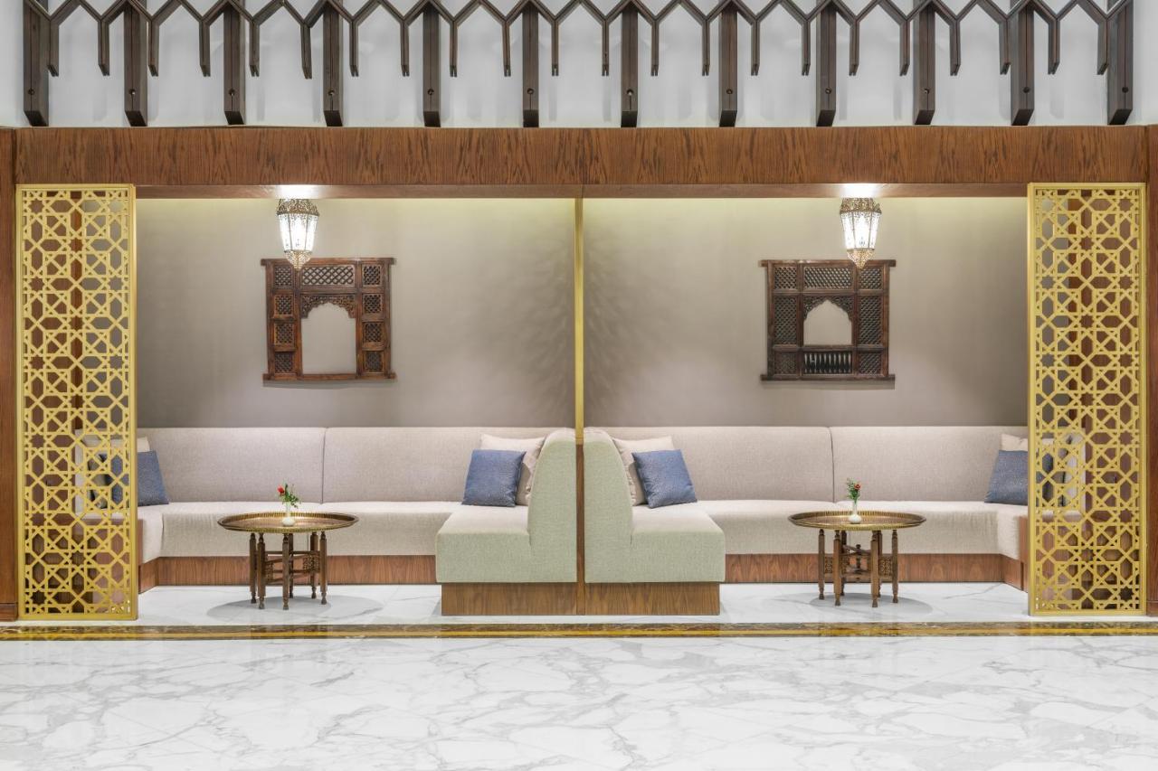 マカレム アイヤッド メッカ ホテル エクステリア 写真 The photo depicts a modern, elegantly designed seating area. It features a pair of sofas with light-colored upholstery, accented by blue cushions. There are several small tables in front of the sofas, likely meant for drinks or decorative items. The 