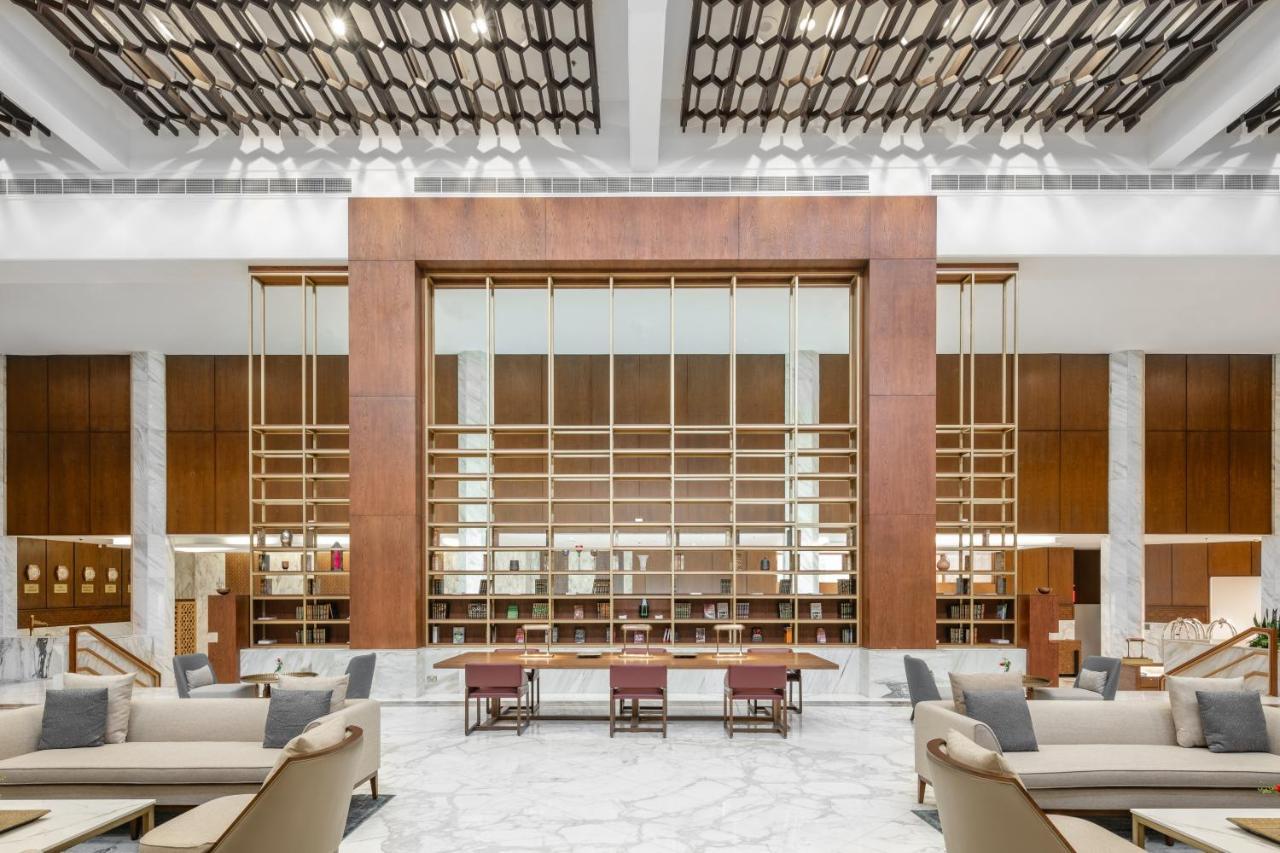 マカレム アイヤッド メッカ ホテル エクステリア 写真 The photo shows a spacious interior of a modern lobby or lounge. The design features a large wooden structure with a grid-like pattern in the center, possibly serving as a decorative partition. The walls are adorned with brown wooden panels, and marb