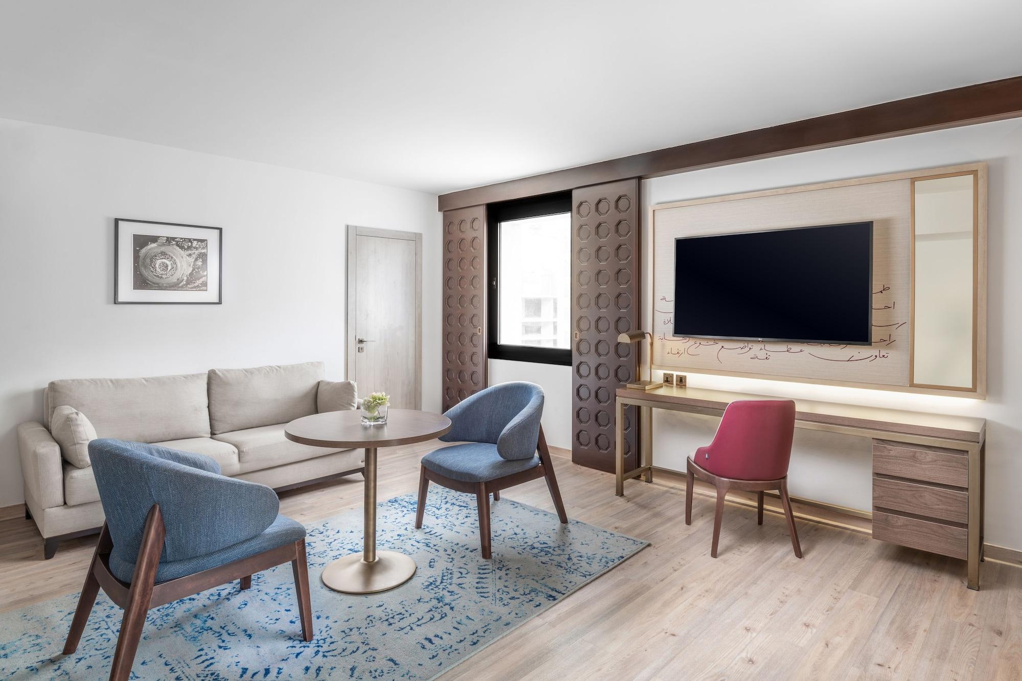 マカレム アイヤッド メッカ ホテル エクステリア 写真 The photo shows a modern living room setting. It features a light-colored sofa positioned against one wall, accompanied by a round table at the center. Two stylish chairs, one in blue and the other in pink, are placed around the table. There is a lar