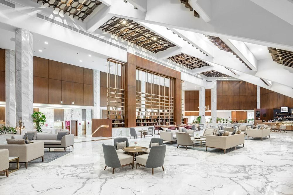 マカレム アイヤッド メッカ ホテル エクステリア 写真 The photo shows a spacious and modern hotel lobby. It features a high ceiling with an elegant design, incorporating wooden accents and contemporary lighting. The floor is made of white marble, creating a bright and open atmosphere. 

In the foregroun