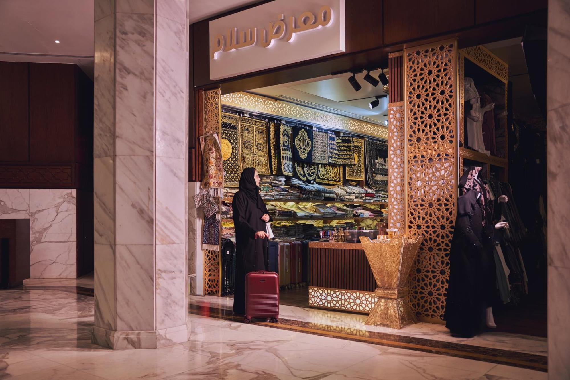 マカレム アイヤッド メッカ ホテル エクステリア 写真 The photo shows a storefront that appears to sell traditional textiles or garments. The entrance features intricate decorative patterns, typical of Middle Eastern architecture. A woman is standing outside the shop, dressed in a black abaya, and she h
