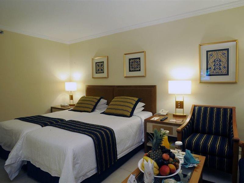 マカレム アイヤッド メッカ ホテル エクステリア 写真 The photo shows a hotel room with a cozy and inviting atmosphere. It features two beds with white linens and dark striped bedspreads. There are two bedside lamps providing warm light, and the walls are decorated with framed artworks. Beside the beds 