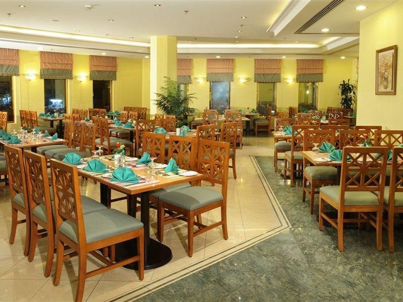 マカレム アイヤッド メッカ ホテル エクステリア 写真 The photo shows an interior view of a restaurant. It features wooden tables and chairs arranged neatly throughout the space. Each table is set with turquoise napkins, contributing to the overall decor. The walls are painted a soft yellow, and there a