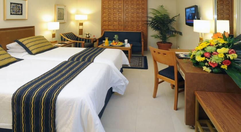 マカレム アイヤッド メッカ ホテル エクステリア 写真 The image shows a hotel room featuring two beds with white linens and a decorative stripe along the edge. There is a seating area with two chairs and a small table, set with a breakfast spread that includes fruit and drinks. A small potted plant adds