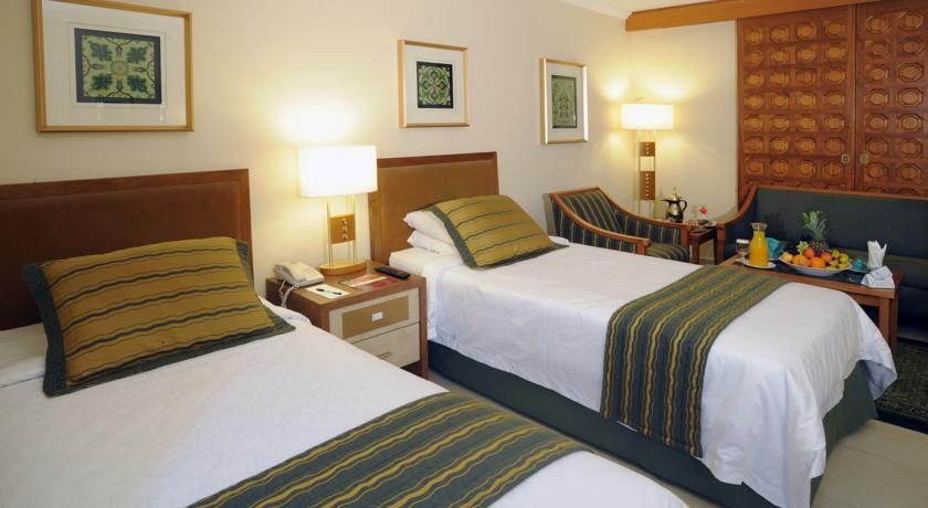 マカレム アイヤッド メッカ ホテル エクステリア 写真 The photo shows a hotel room with two twin beds, each topped with decorative green and gold striped bed runners. There is a nightstand between the beds with a lamp on it. The room features light-colored walls, framed artwork on the walls, and a small